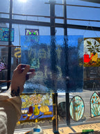 Hand holding a blue rectangular sheet of glass in front of stained glass windows