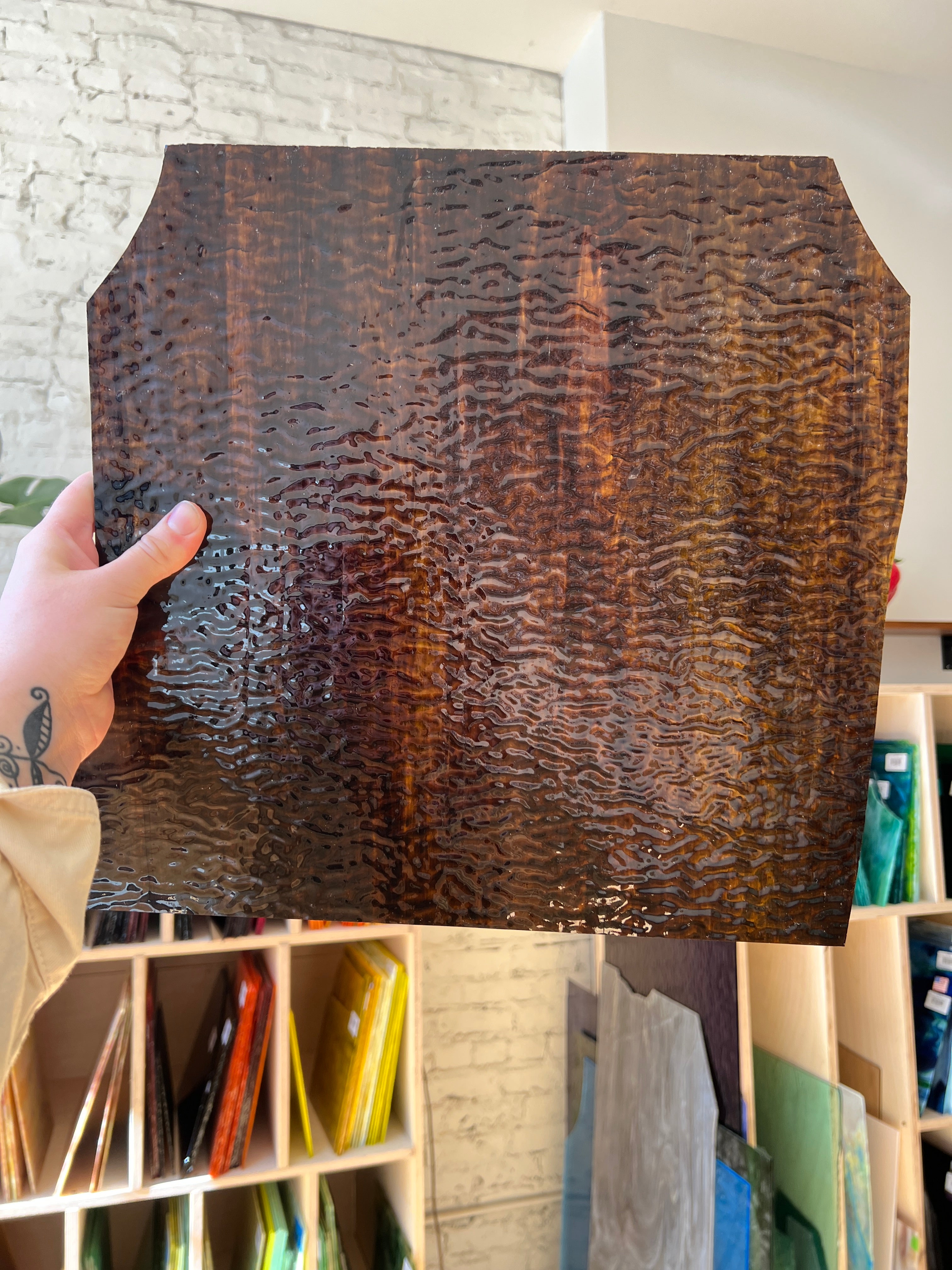 Hand holding a textured brown piece of stained glass with a blurred indoor setting in the background