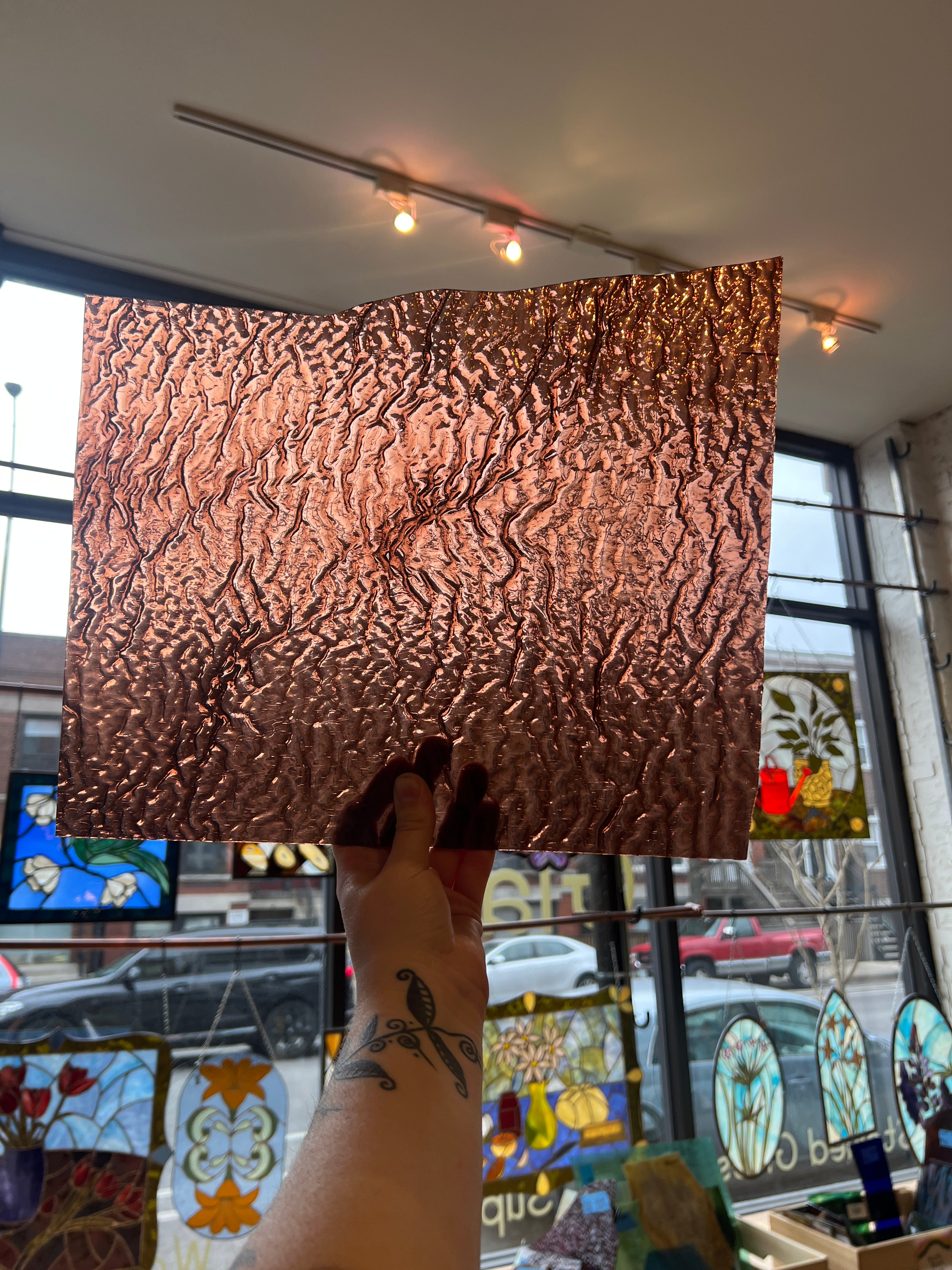 Person holding a textured bronze-colored panel of glass in front of a colorful stained glass window.