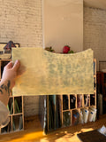 Person holding an off white mottled piece of stained glass in front of a blurred sunny interior. 
