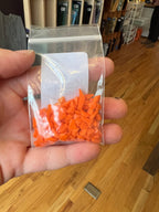 Hand holding a clear plastic bag with orange frit against a wooden floor background