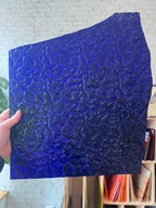 Blue textured sheet of stained glass held by a hand with a blurred indoor background