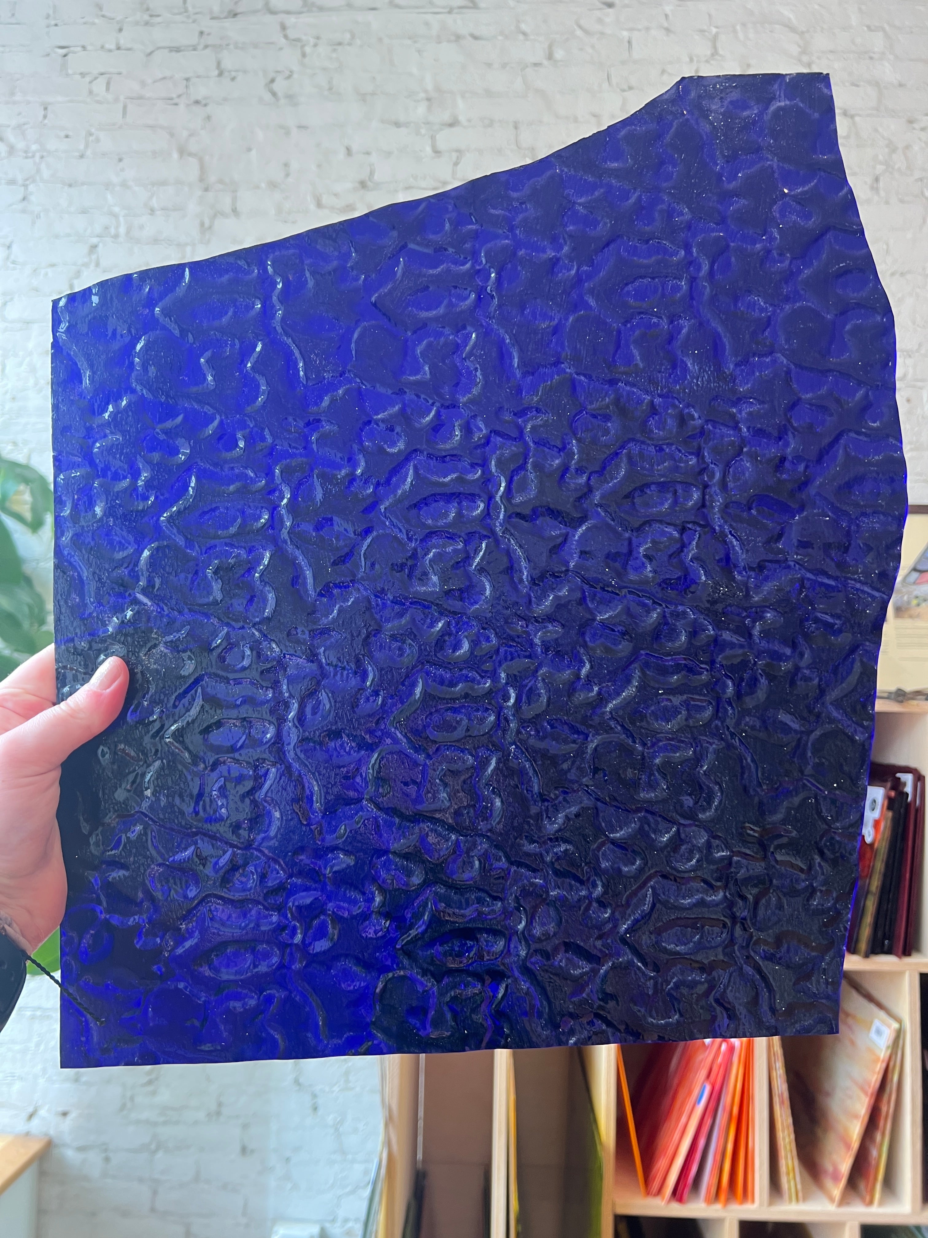 Blue textured sheet of stained glass held by a hand with a blurred indoor background
