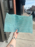 Person holding a teal textured sheet of stained glass outdoors on a city street.