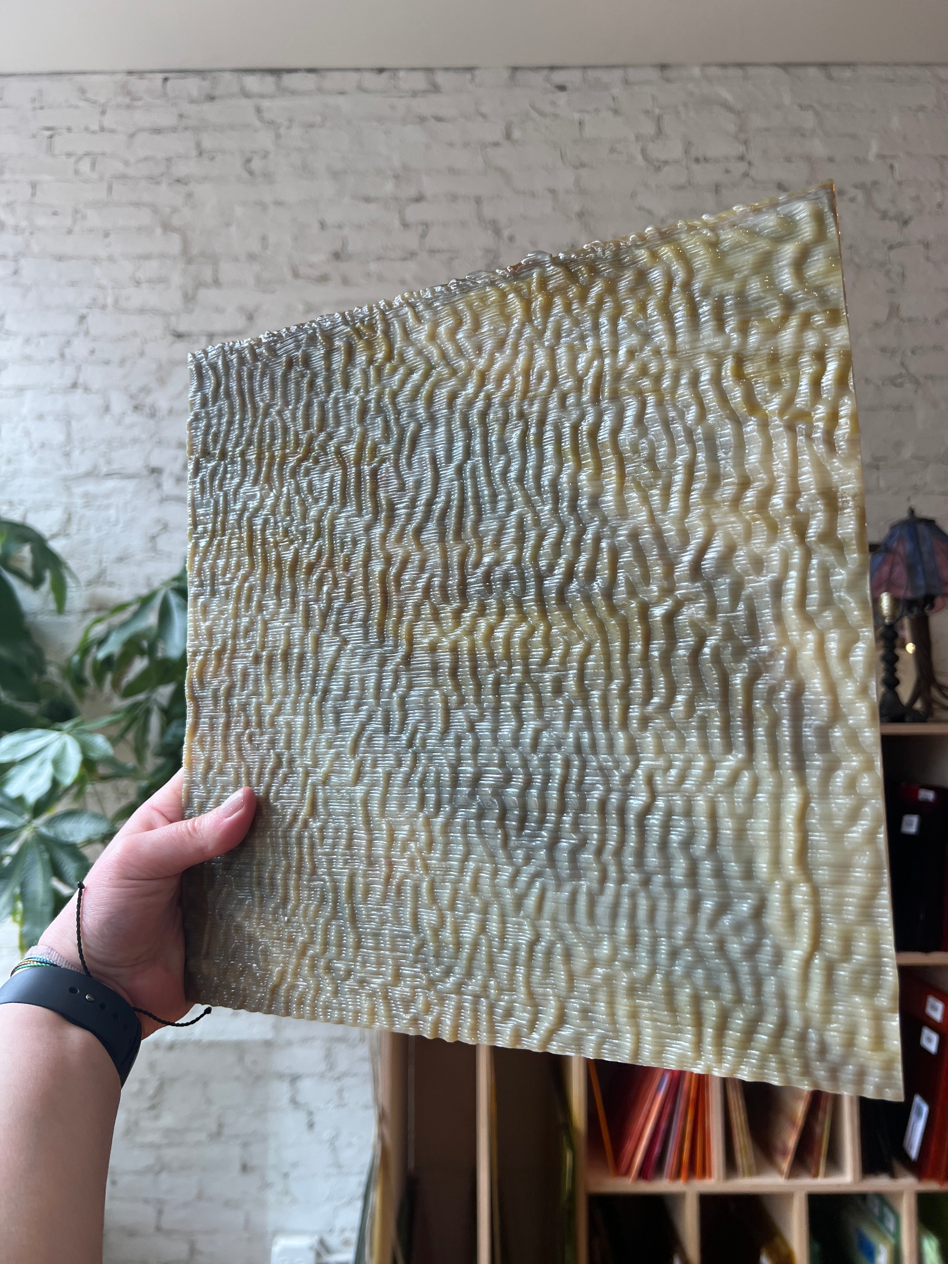 Hand holding a textured brown panel of stained glass with anwavy pattern against a blurred indoor background