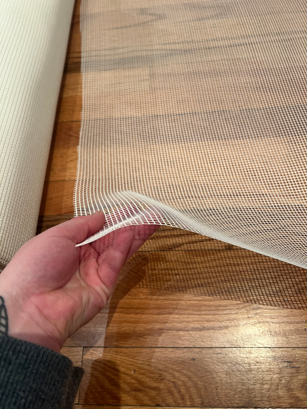 Hand holding a piece of white mesh against a wooden surface