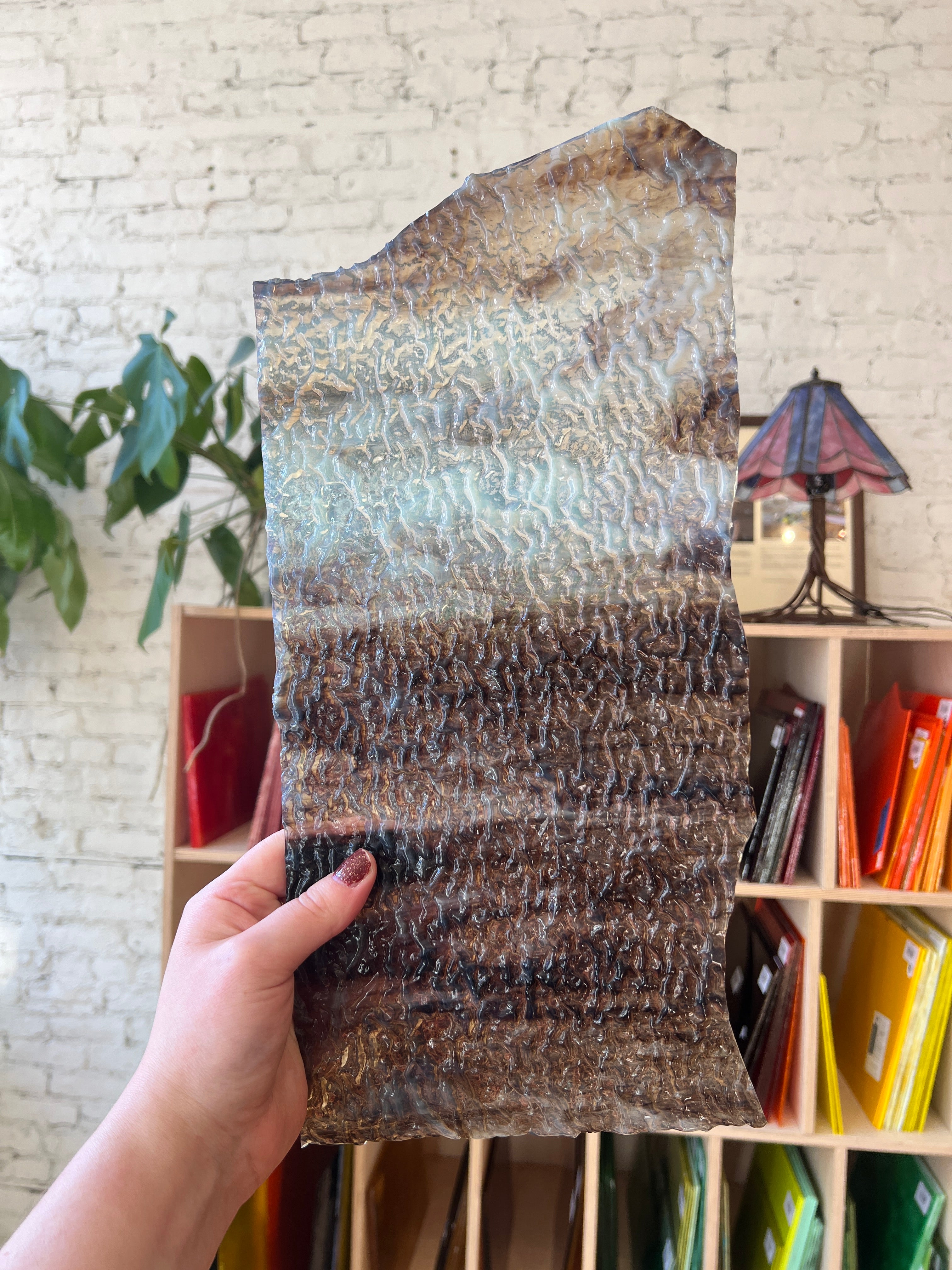 Person holding a piece of textured brown stained glass with a blurred indoor background