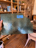 Glass sheet held up in front of a room with wooden floors and shelves.