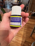 Hand holding a small bottle with a label against a blurred indoor background