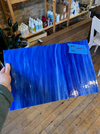 Person holding a large blue sheet of glass with a label in an indoor setting