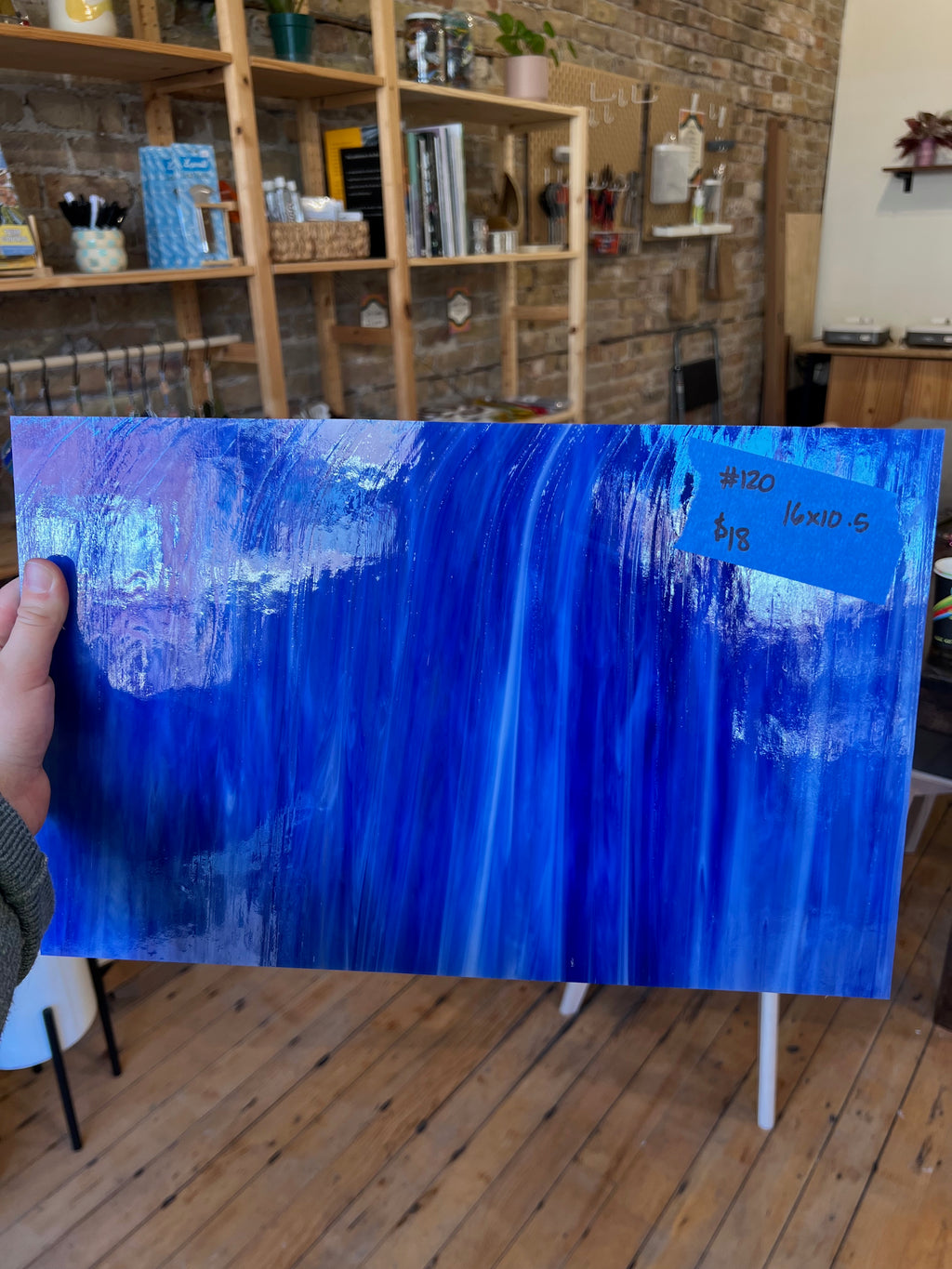 Person holding a large blue abstract glass sheet indoors.