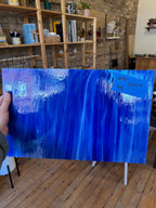 Person holding a large blue abstract glass sheet indoors.