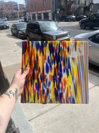 Colorful piece of stained glass held by a hand in an urban street setting