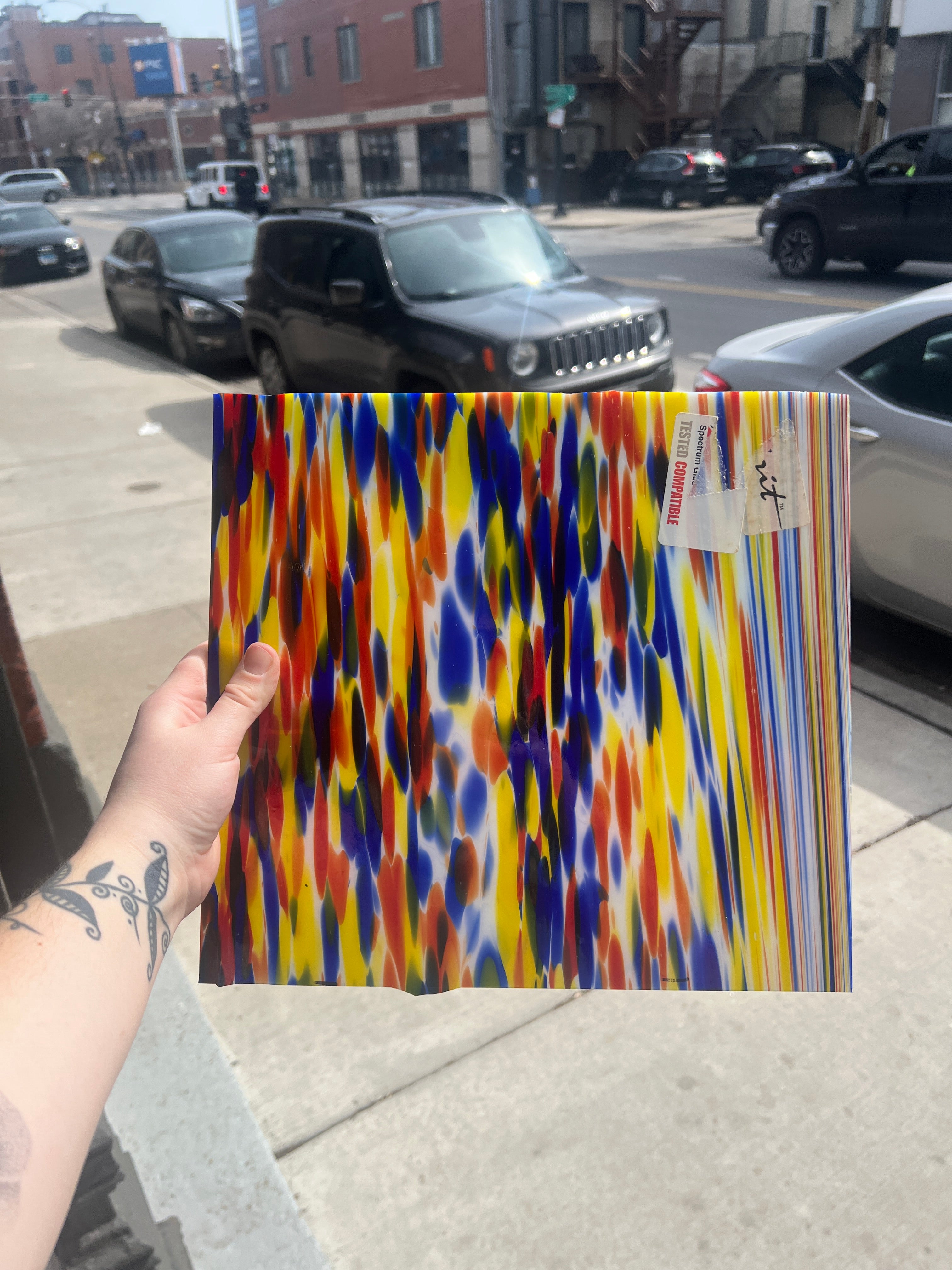Colorful piece of stained glass held by a hand in an urban street setting