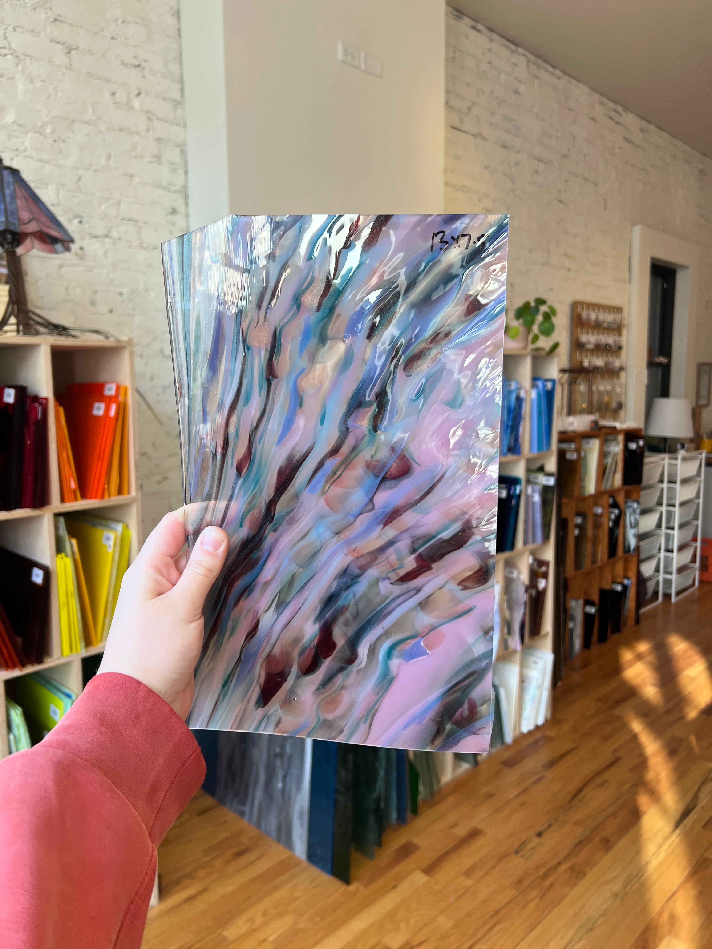 Person holding a colorful abstract piece of stained glass in an art store.