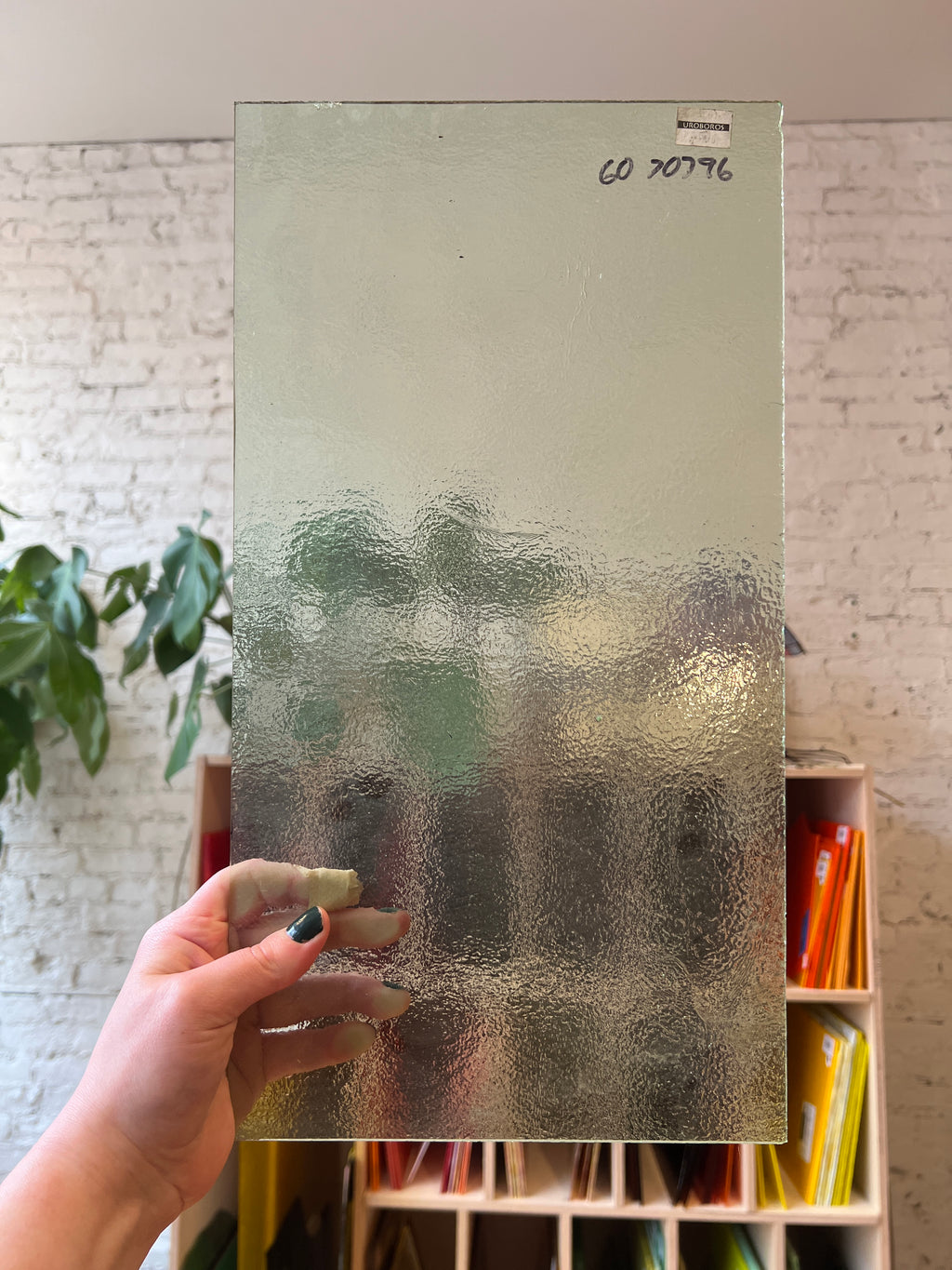 Hand holding a textured piece of clear stained glass with a blurred background