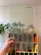 Hand holding a textured piece of clear stained glass with a blurred background