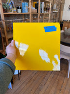 Hand holding a yellow piece of glass in a room with wooden flooring and furniture.