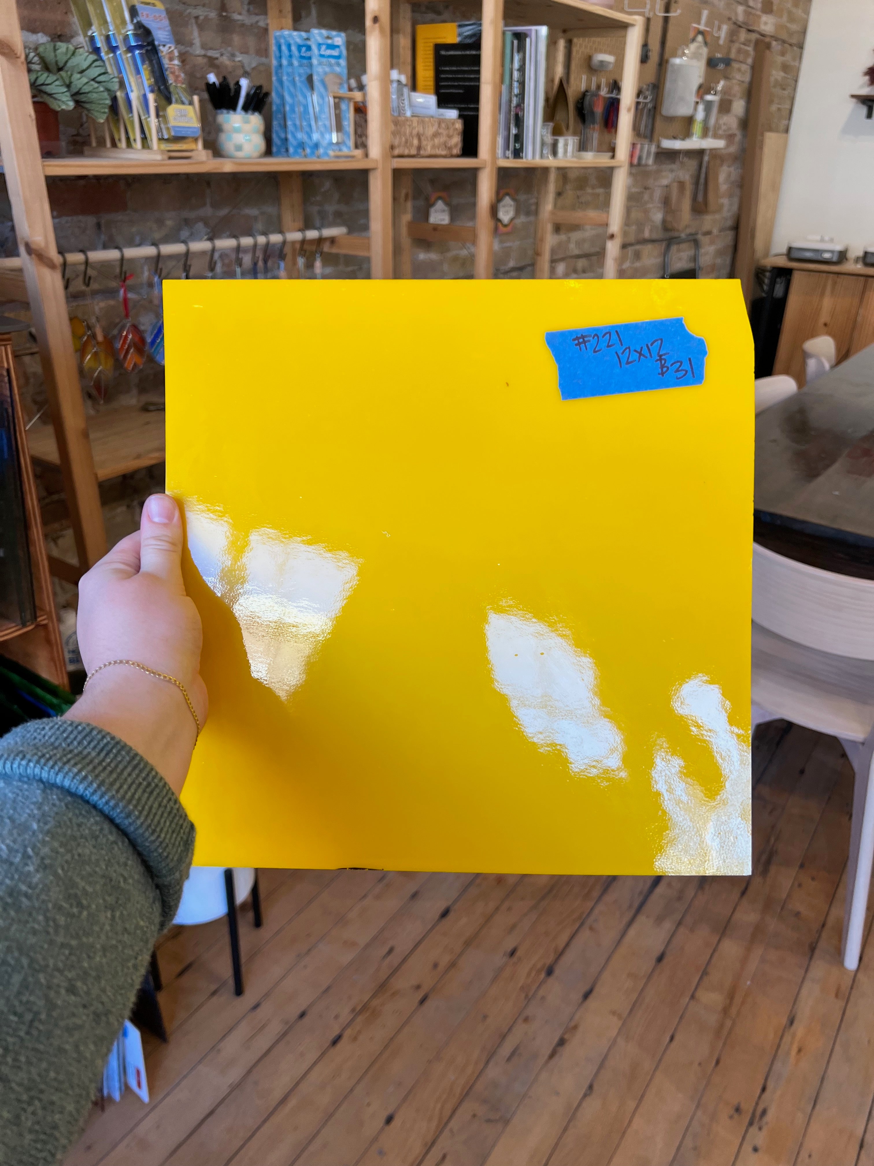 Hand holding a yellow piece of glass in a room with wooden flooring and furniture.