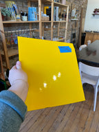 Hand holding a yellow sheet of glass with a blue label in an indoor setting