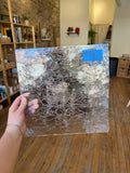 Person holding a textured glass panel with a blue label in an indoor setting.