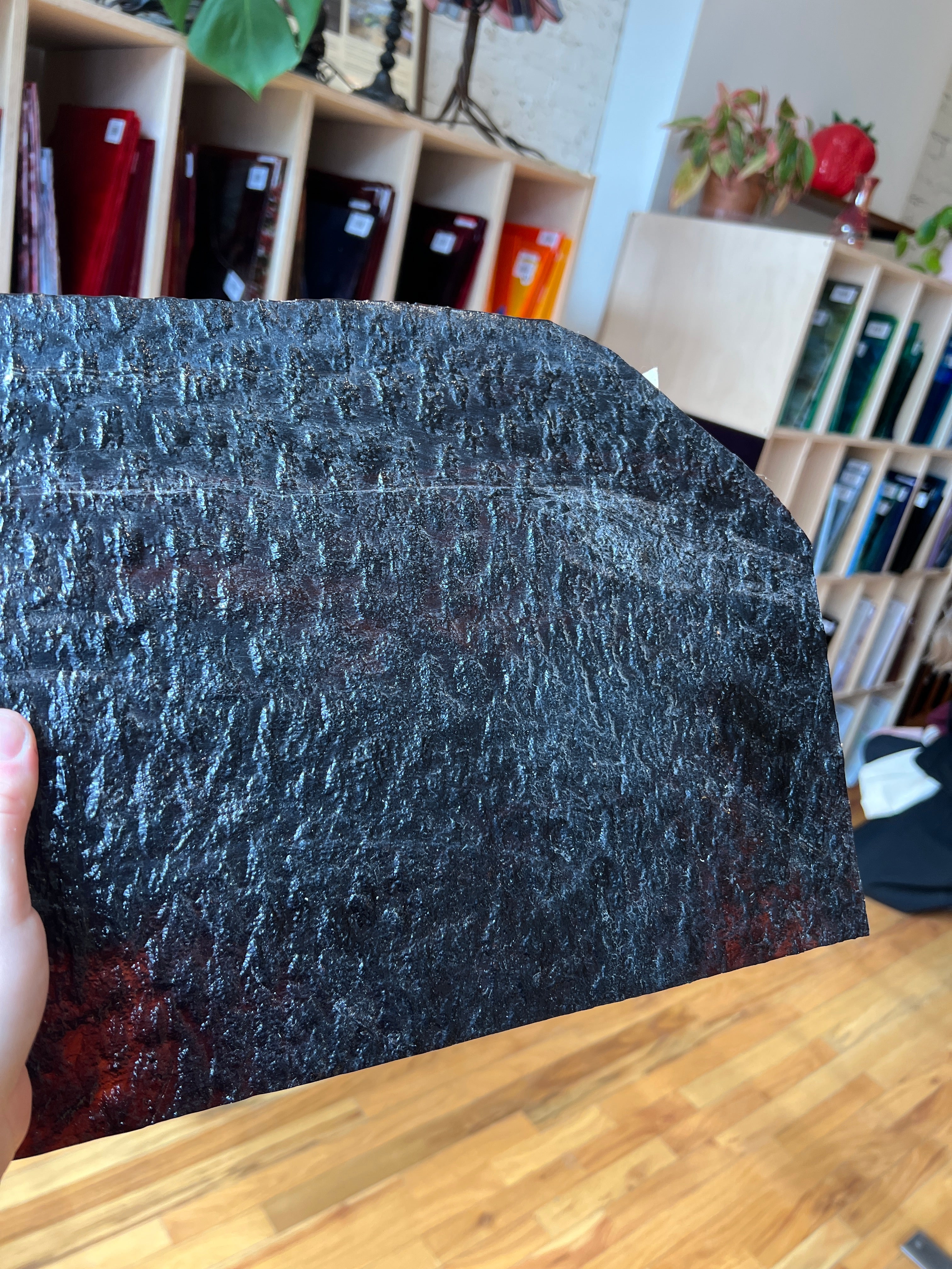 Close-up of a textured black piece of stained glass held by a hand, with a blurred indoor background.