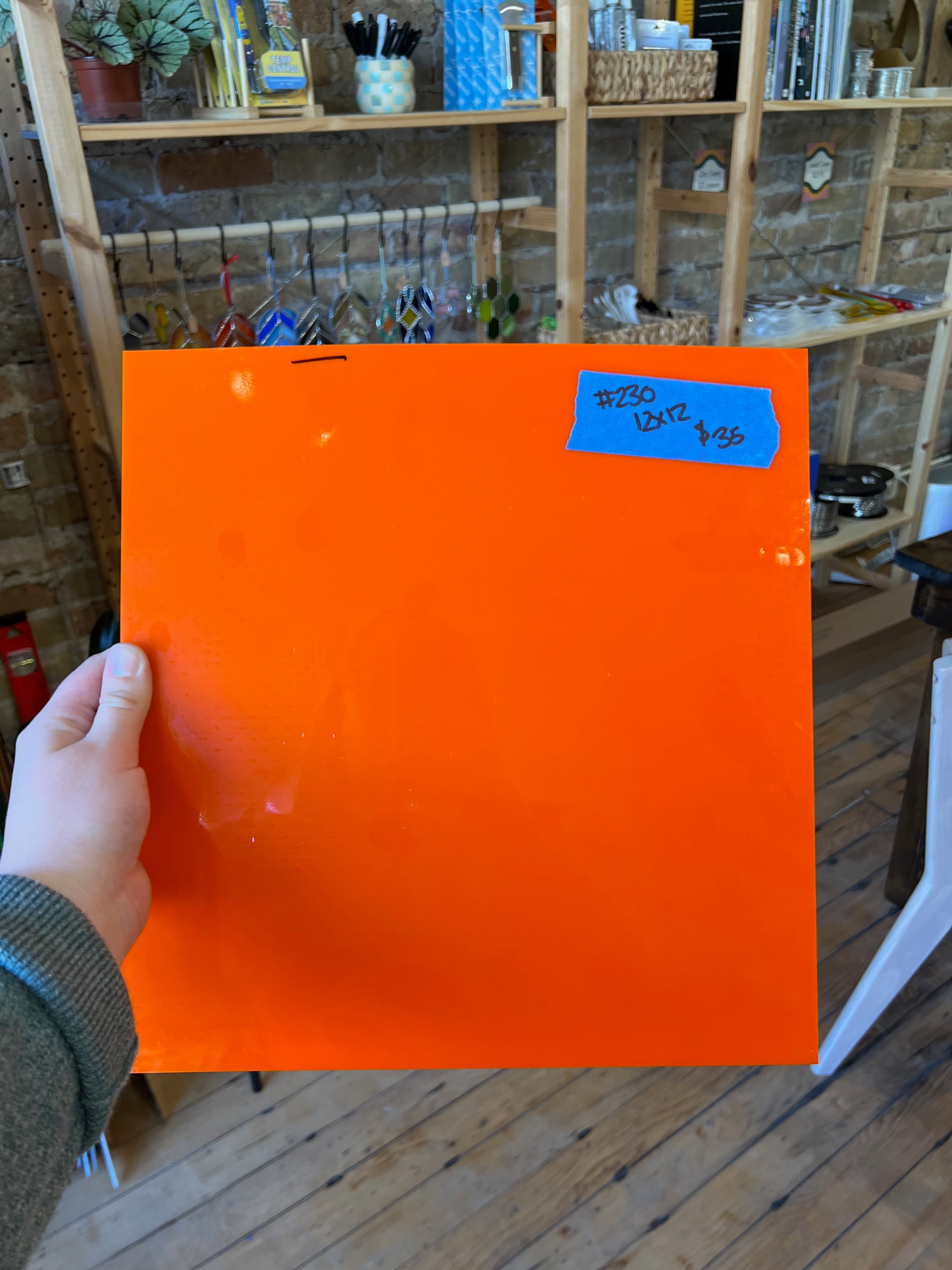 Orange sheet of glass held by a hand with a blue price tag in a store setting