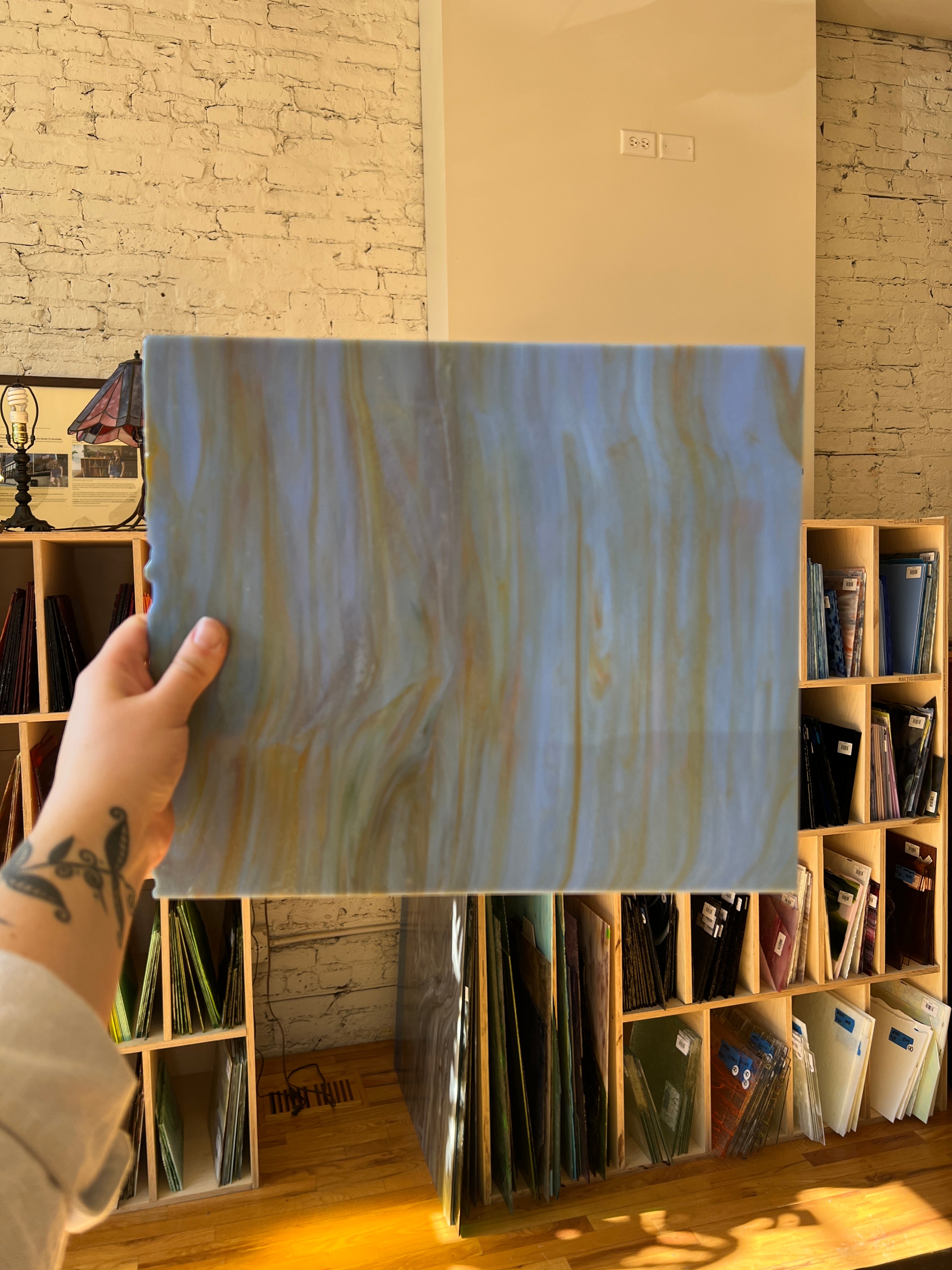 Person holding a great swirled piece of stained glass in front of a blurred sunny interior.