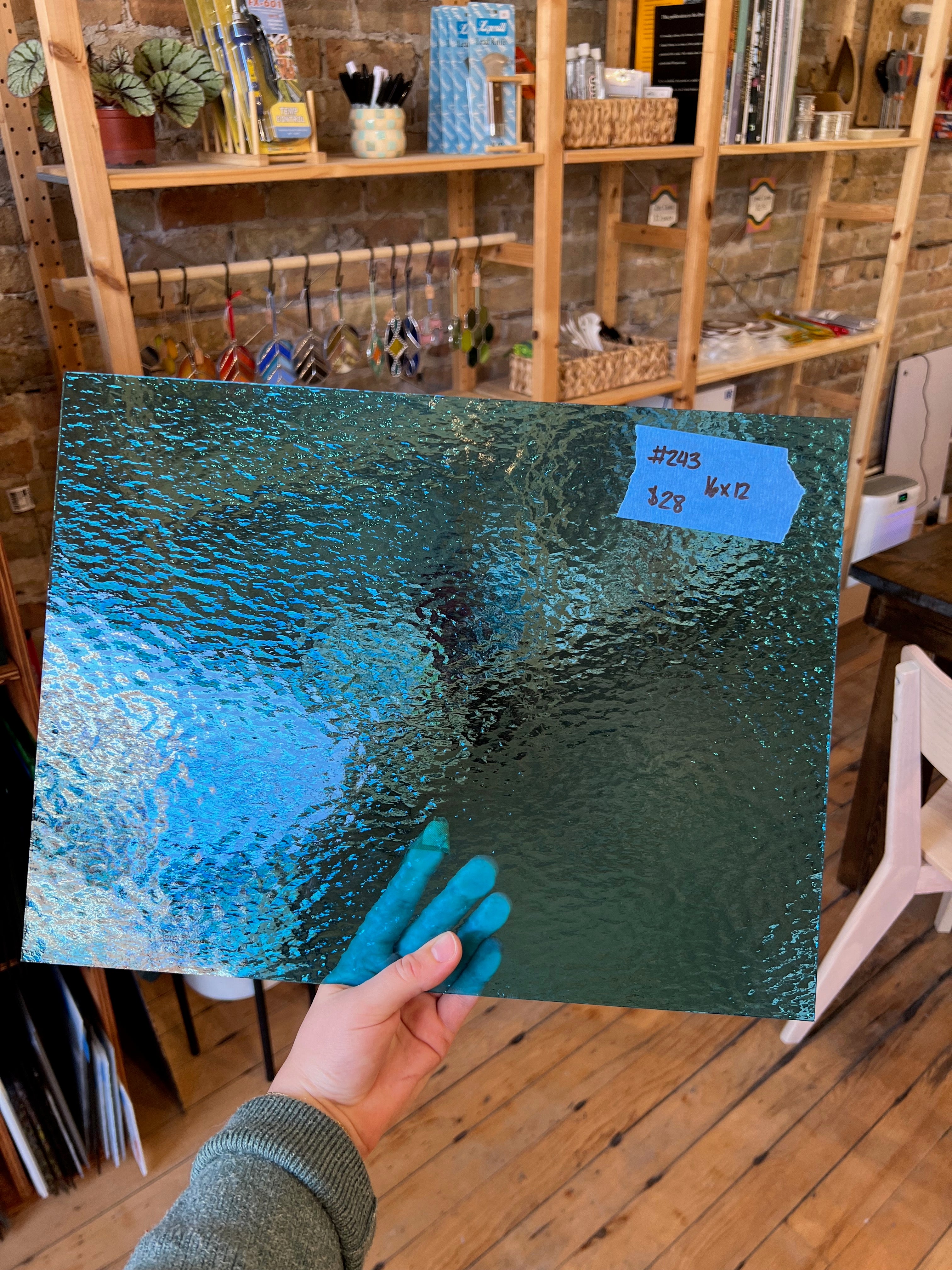 Person holding a textured blue and green panel of glass with a blurred indoor setting in the background