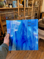 Hand holding a blue piece of glass in a room with shelves and decor.