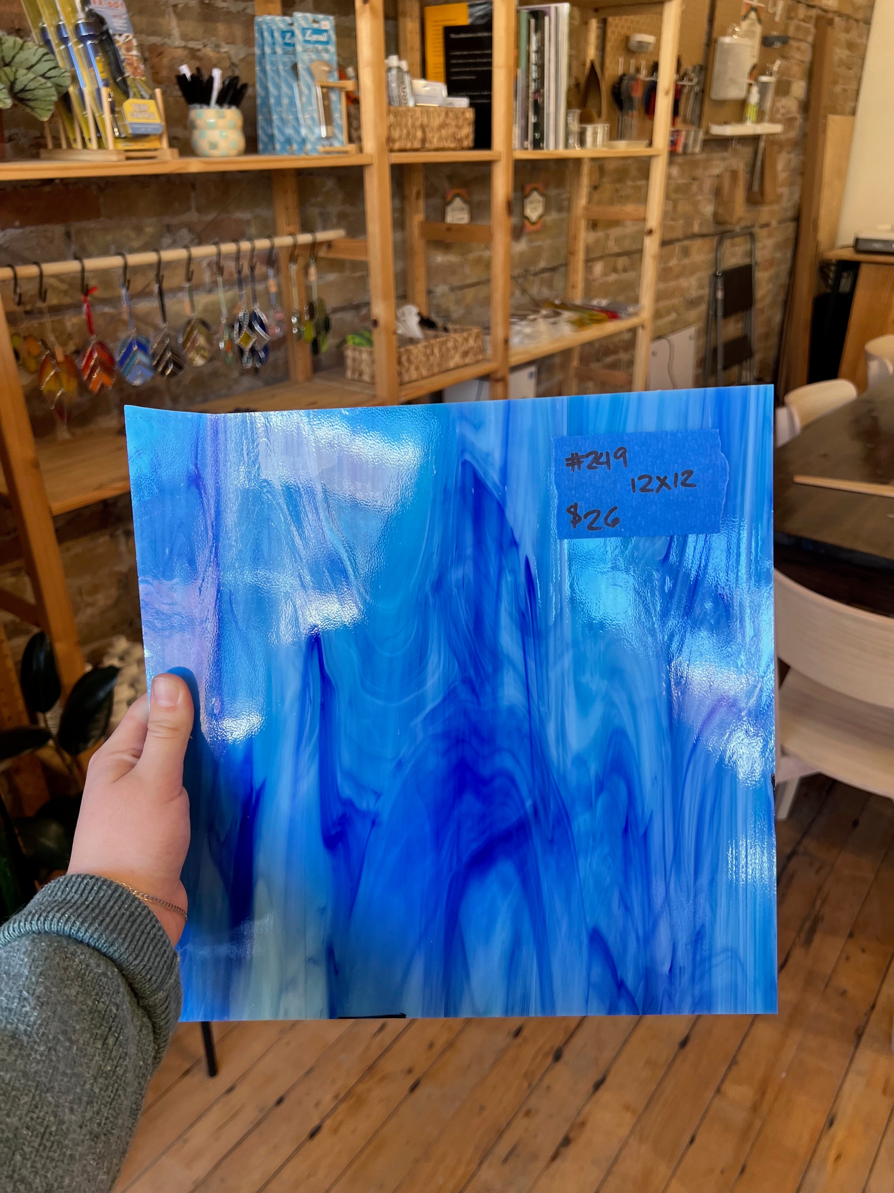 Hand holding a blue piece of glass in a room with shelves and decor.