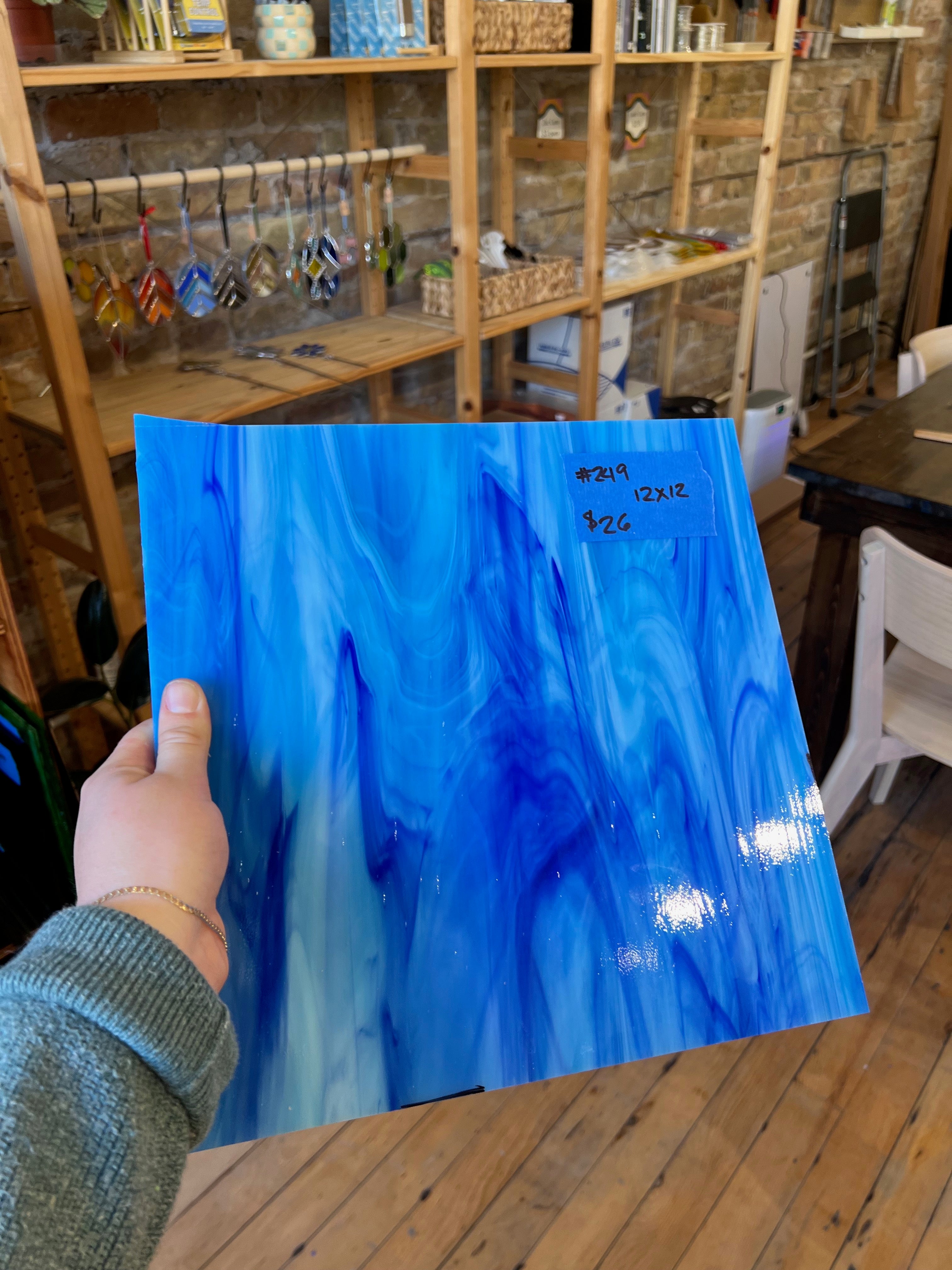Person holding a blue marbled piece of glass in a rustic setting with wooden shelves and furniture.