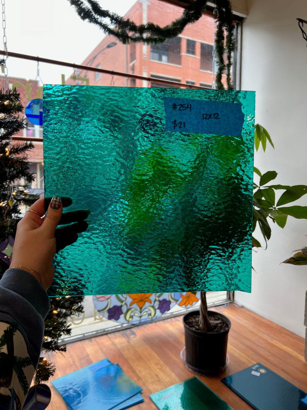 Person holding a piece of teal textured glass in a room with plants and a window.