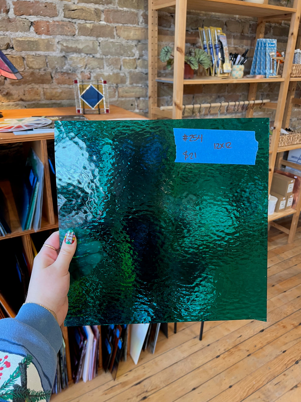 Person holding a green textured piece of glass in front of a bookshelf.