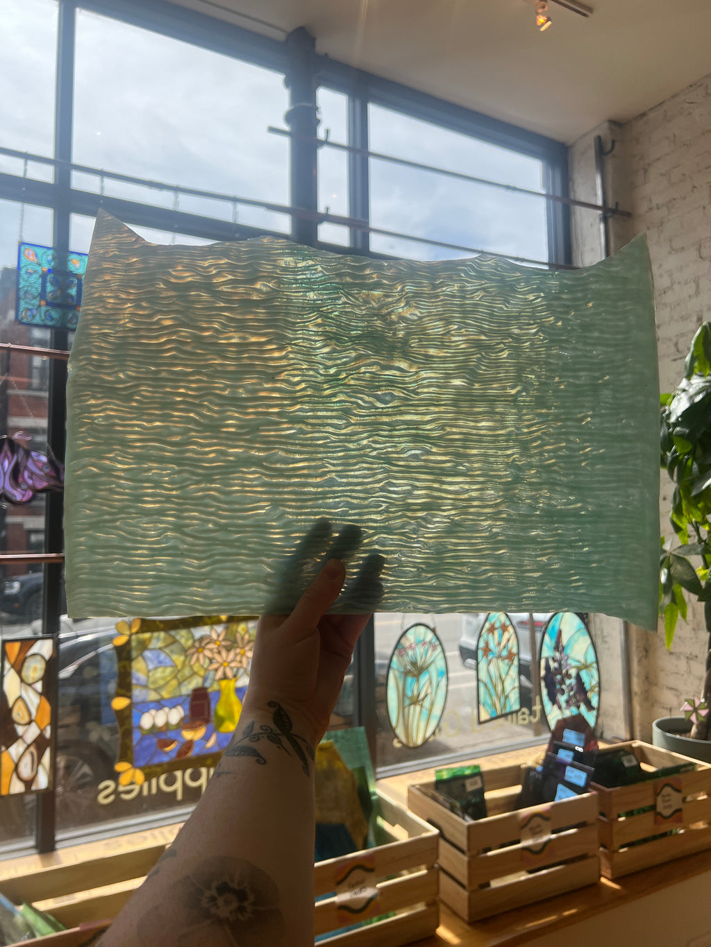 Person holding a green textured piece of glass in front of a window with stained glass