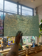 Person holding a green textured piece of glass in front of a window with stained glass