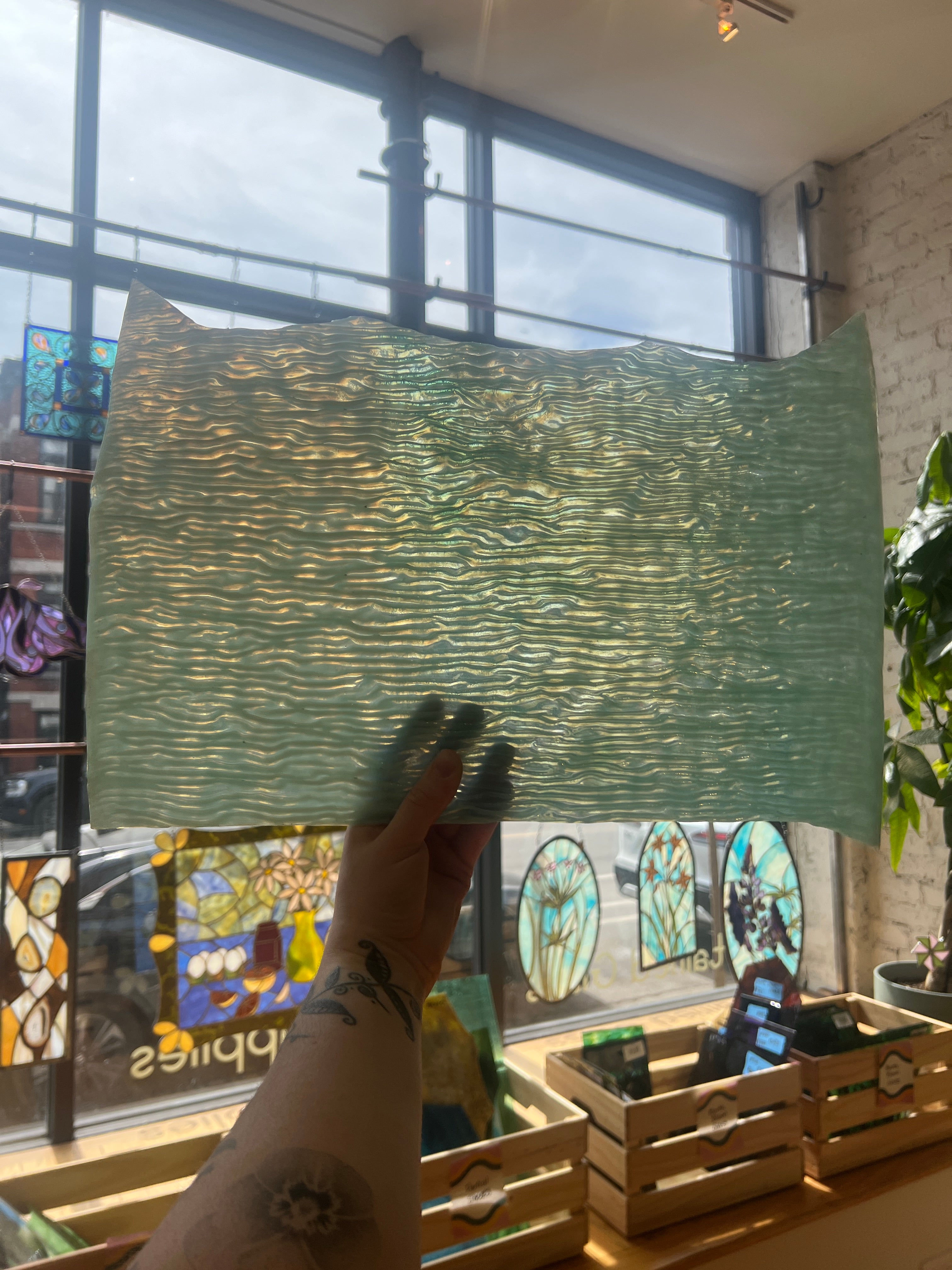 Person holding a green textured piece of glass in front of a window with stained glass