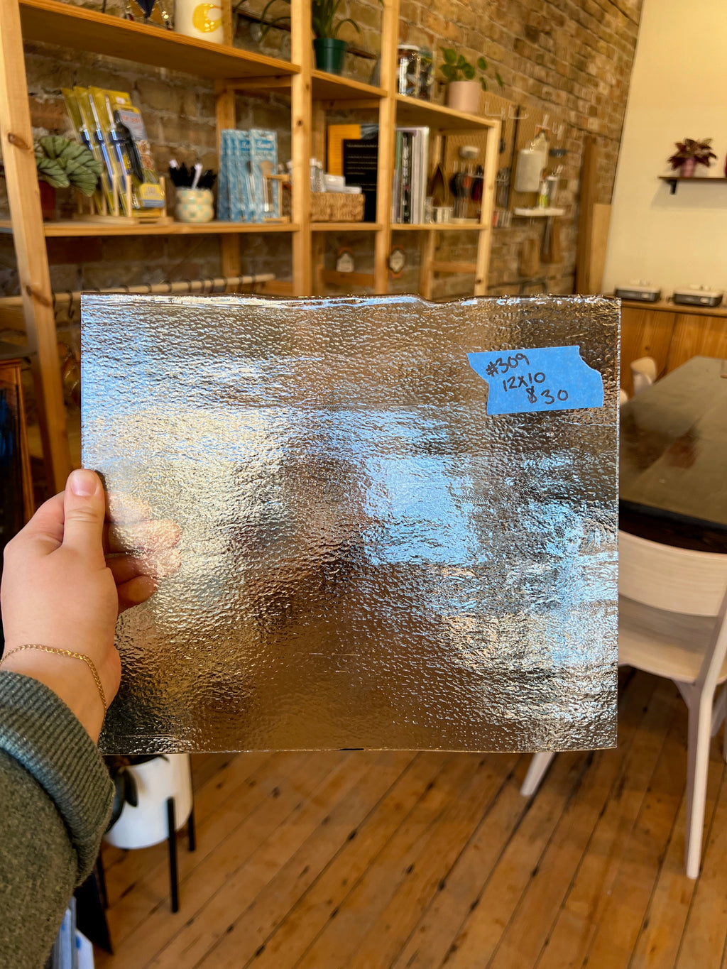 Person holding a textured glass sheet with a blurred indoor setting in the background
