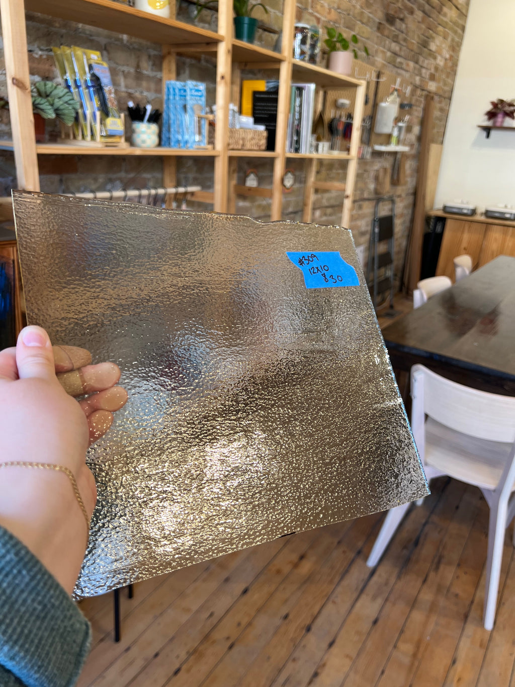 Person holding a sheet of glass in a room with wooden shelves and furniture.