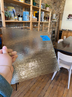 Person holding a sheet of glass in a room with wooden shelves and furniture.