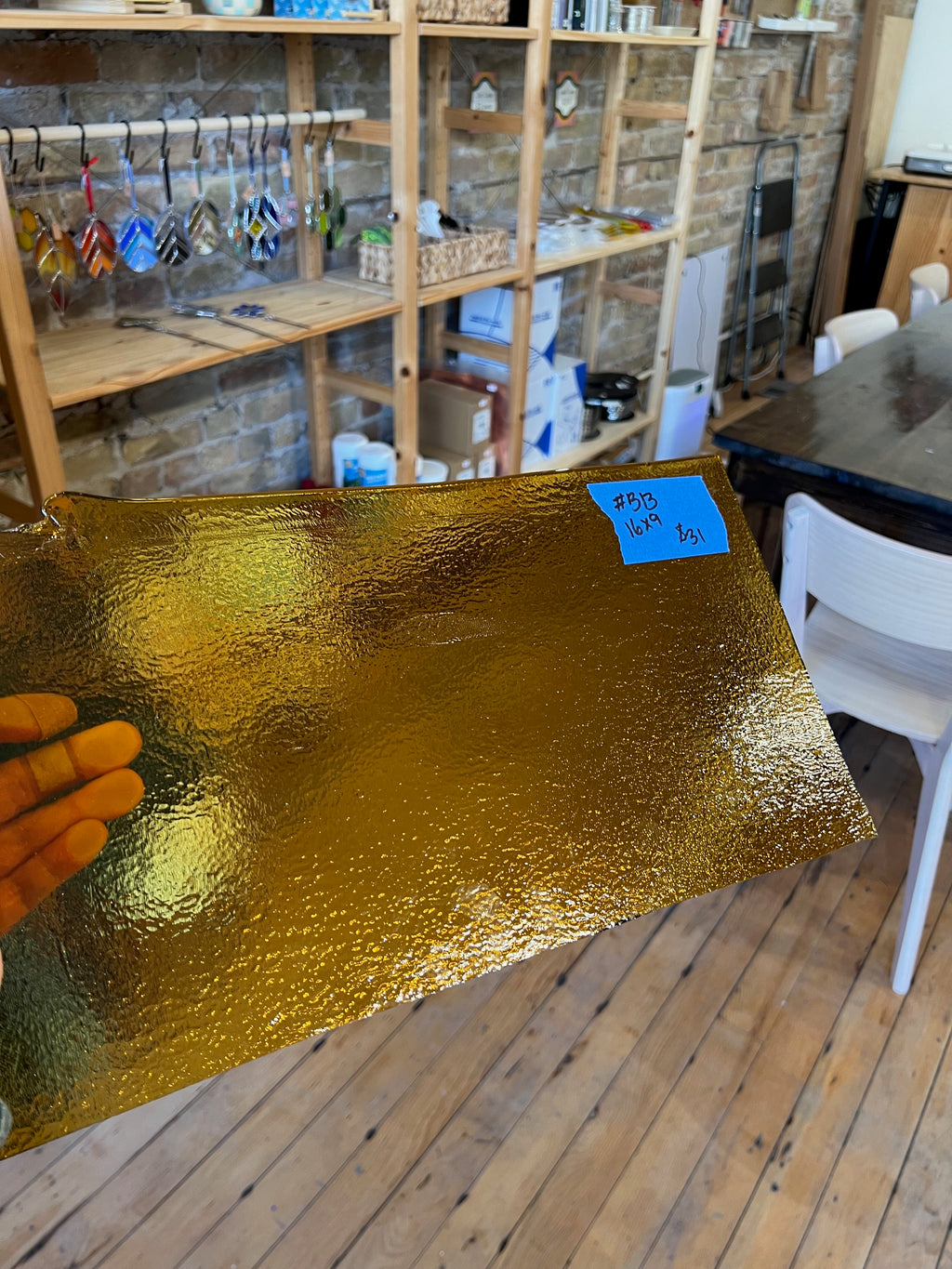 Gold glass sheet held up in front of a room with wooden shelves and a table.
