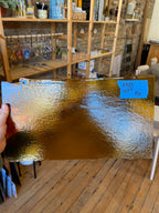 Gold glass sheet held by a hand with a blurred indoor setting in the background