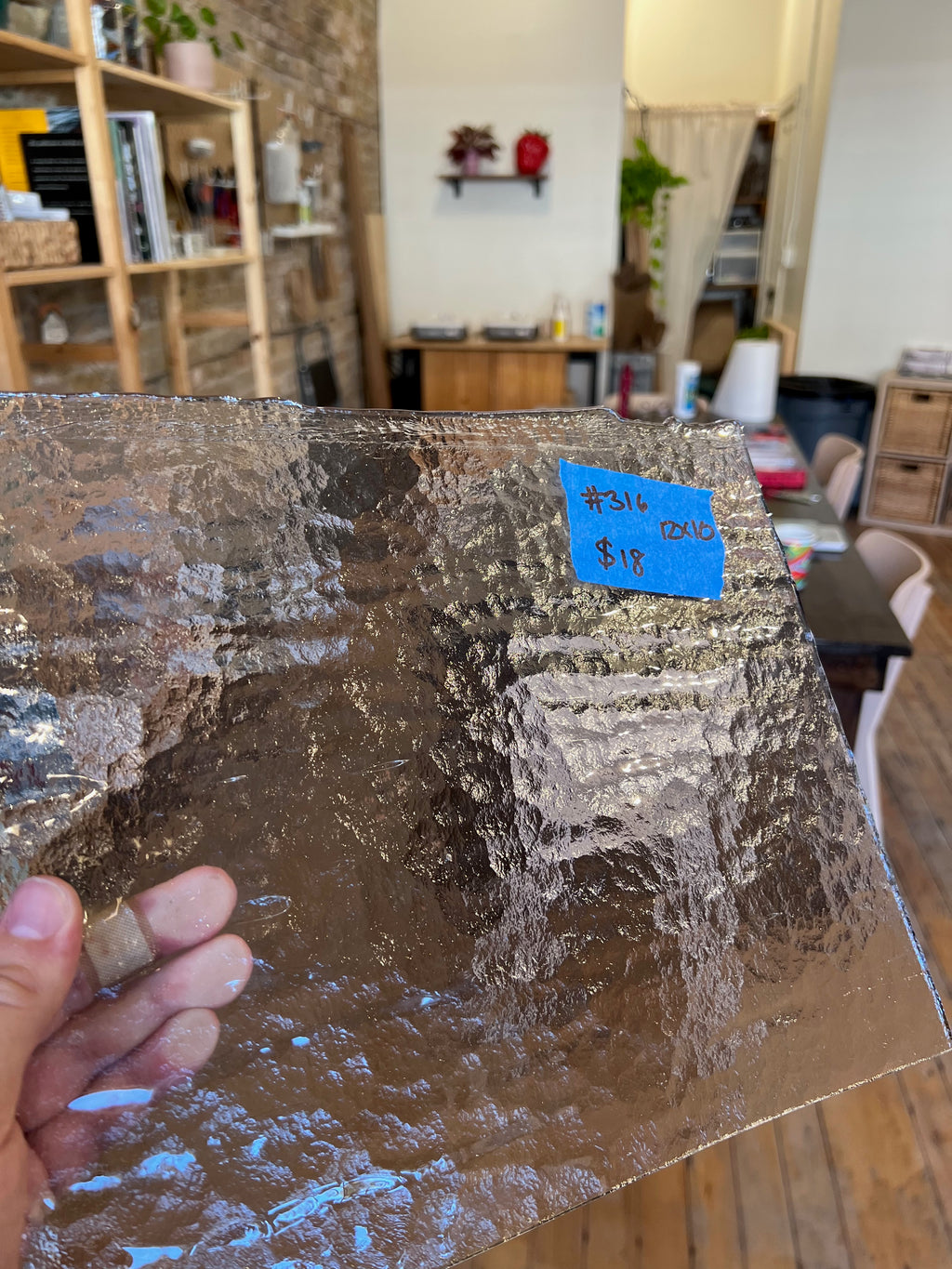Glass sheet with text and a blue label held by a hand in a room setting.
