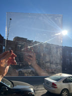 Person holding a lightly textured piece of transparent glass with a cityscape and car in the background