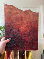 Hand holding a textured red piece of stained glass against a neutral background