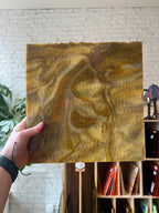 Hand holding a piece of brown stained glass with a marbled pattern against a textured wall.
