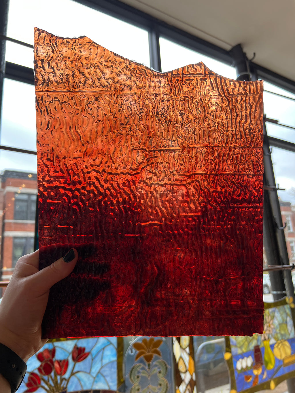 Textured red and orange panel piece of glass held by a hand with a stained glass window in the background
