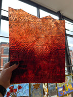 Textured red and orange panel piece of glass held by a hand with a stained glass window in the background