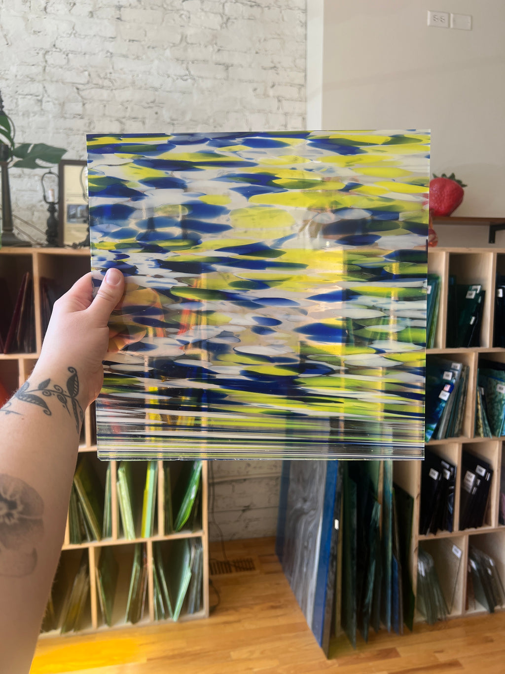 Person holding a colorful piece of stained glass in a room with bookshelves.