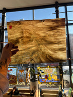 Person holding a piece of brown swirled stained glass in front of a bright blurred window. 